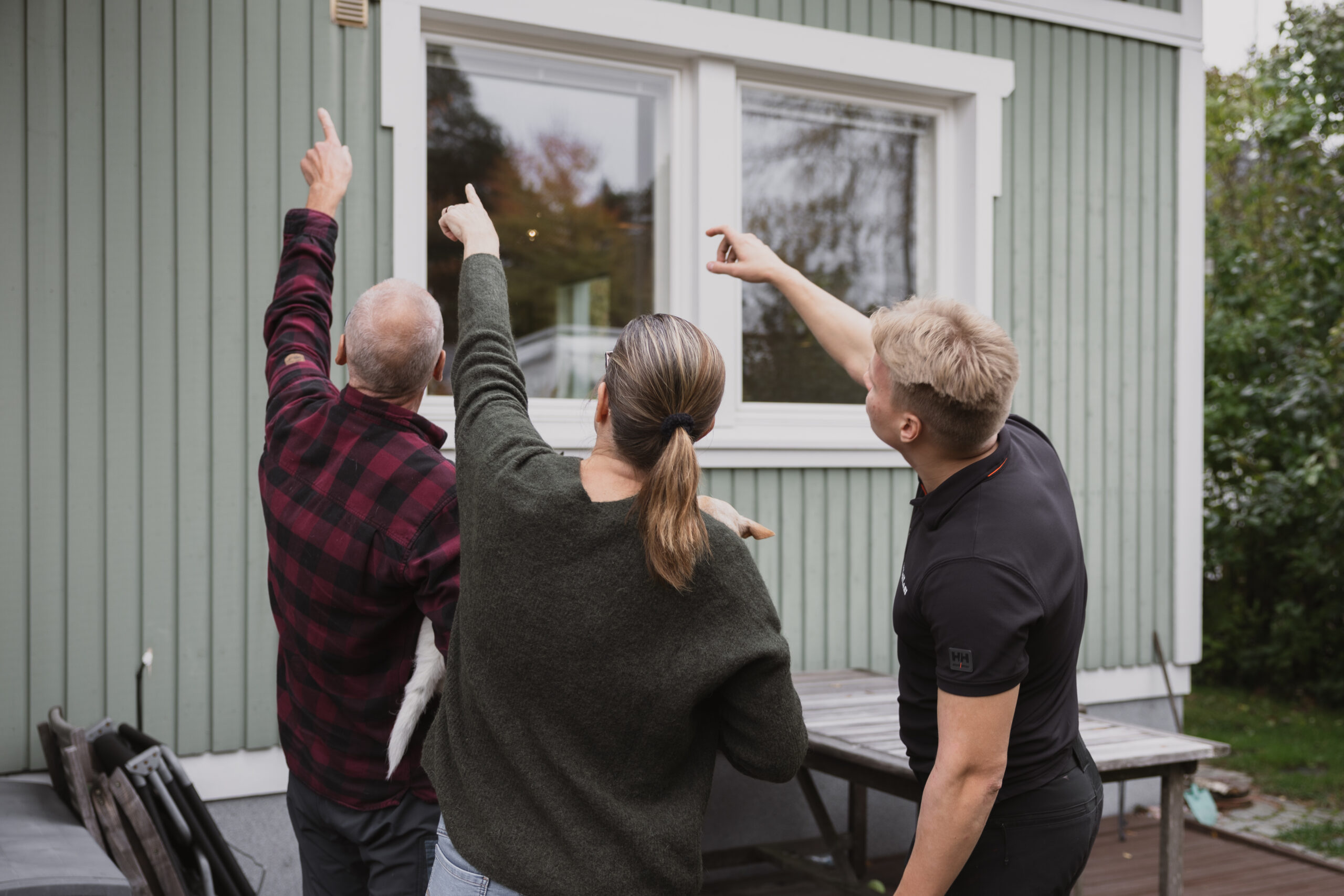 Kilpilasin asiantuntija ja asukkaat katsovat omakotitalon ikkunoiden kuntoa pihalla